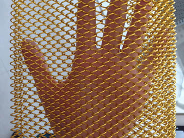 A piece of golden coil drapery mesh and a hand behind it
