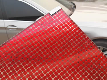 A corner of laminated glass wire mesh with red metal fabric inter-layer is beside a silver white car.