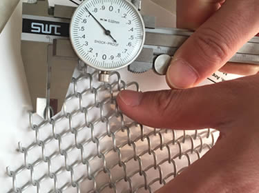 The wire diameter of a white coil drapery is measured by a caliper.