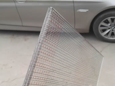 A corner of laminated glass wire mesh with unique woven type wire mesh inter-layer is beside a silver white car.
