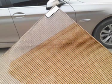 A corner of laminated glass wire mesh with copper cable mesh inter-layer is beside a silver white car.