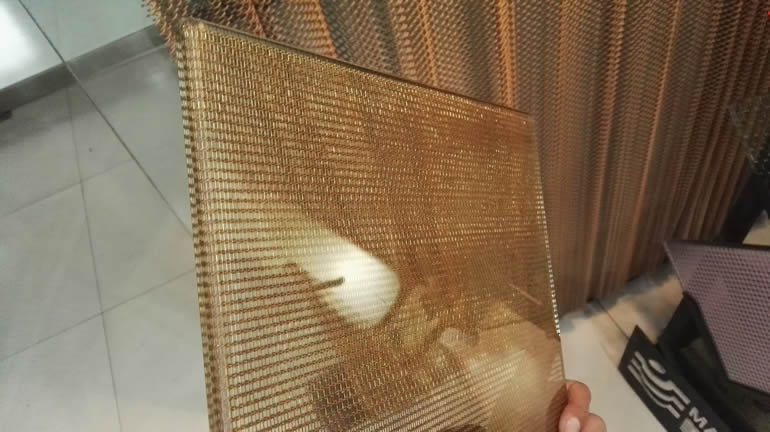 A piece of laminated glass wire mesh with embedded brass cable mesh is beside a coil drapery curtain.