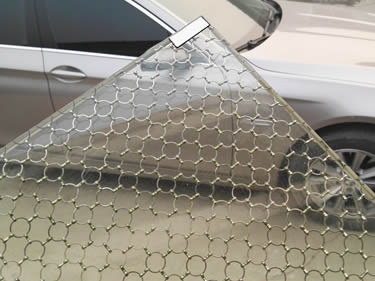 A corner of laminated glass wire mesh with ring mesh inter-layer is beside a silver white car.
